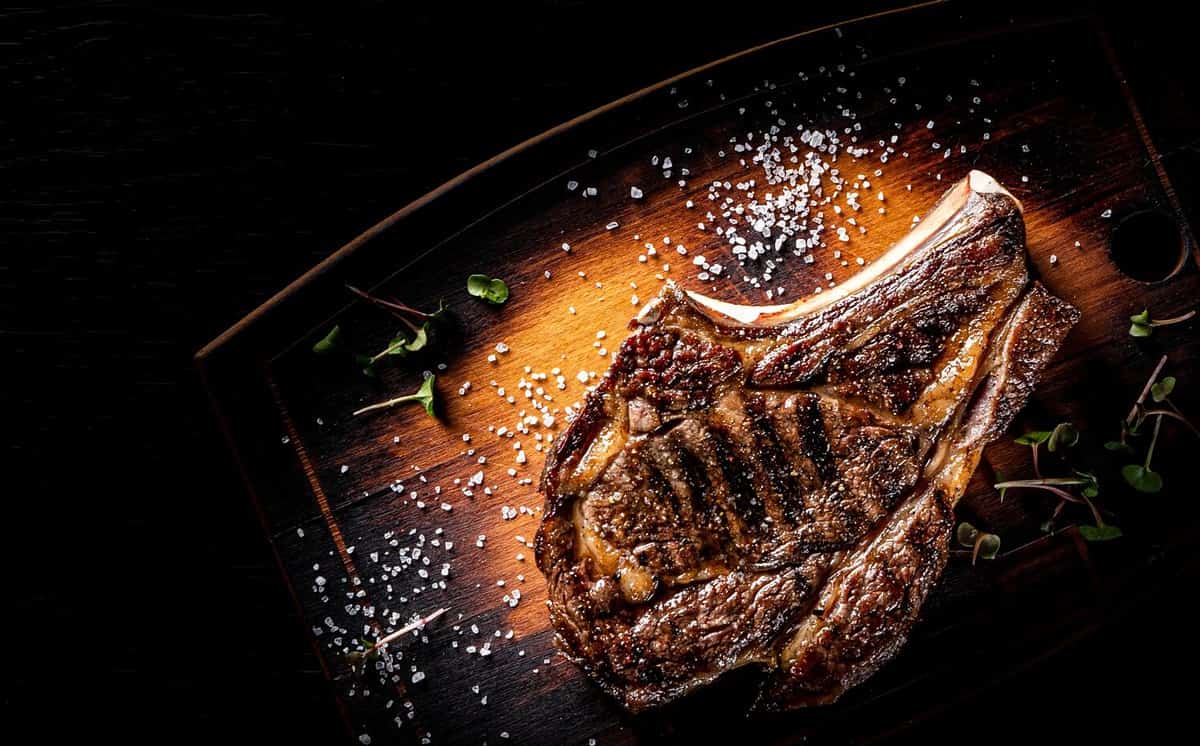 Grilled Ribeye Steak on bones on wooden board, prime cowboy steak on dark background