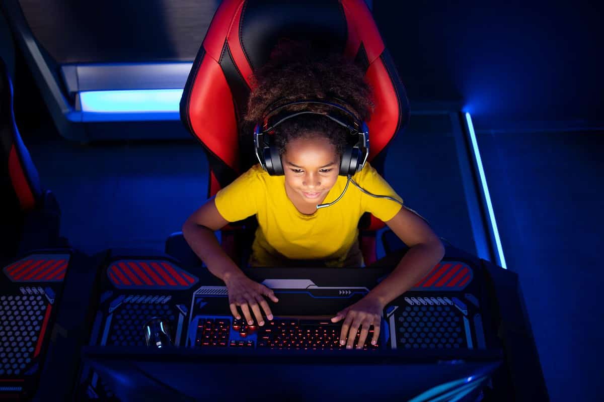 Top view of African American girl gamer playing video games on computer in game room. Children's addiction to virtual games and entertainment.