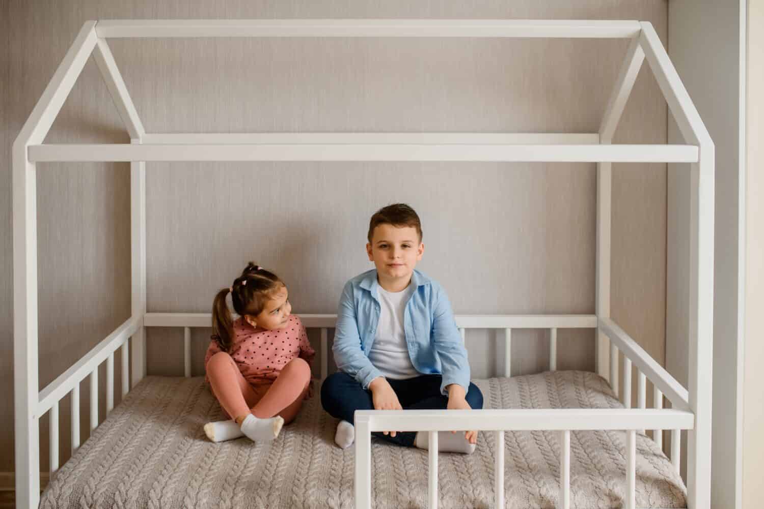 Two Children brother and sister are sitting in a Montessori bed and looking at each other. Bed for kids in a house shape.