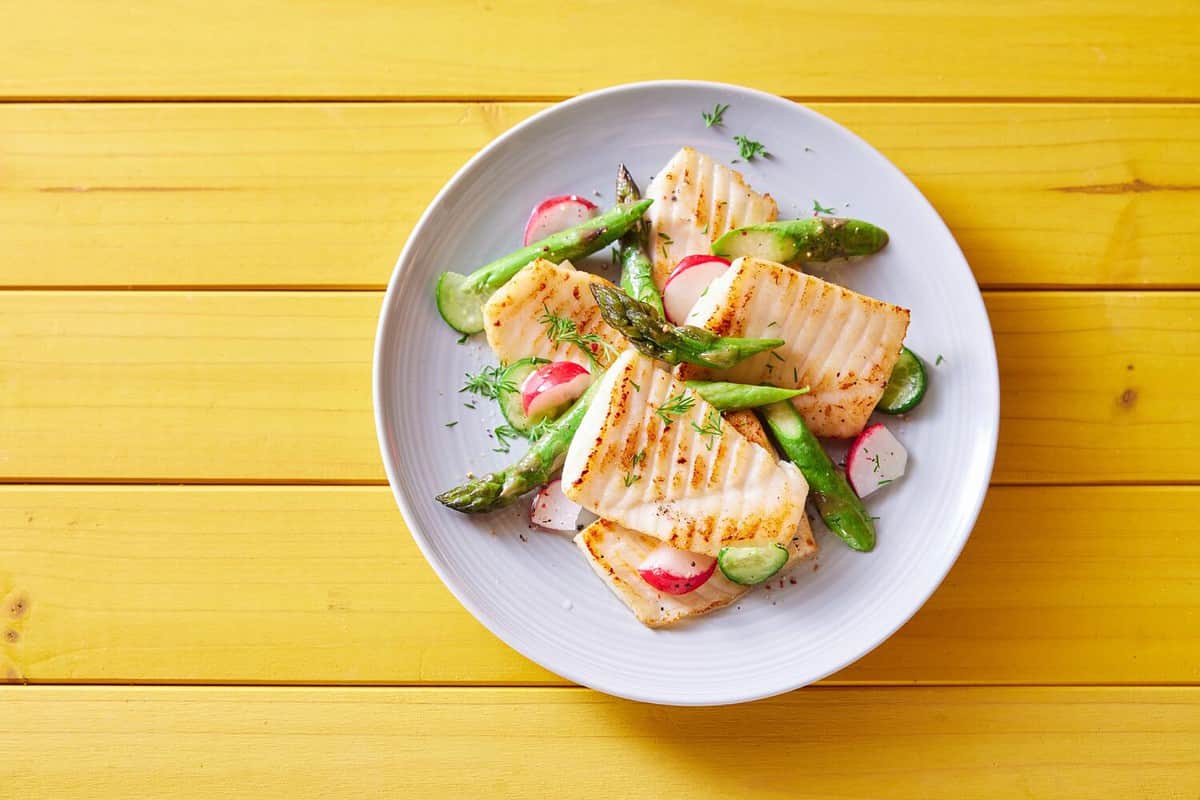 Top view of palatable grilled tilapia fish with cut vegetables served on plate on wooden table