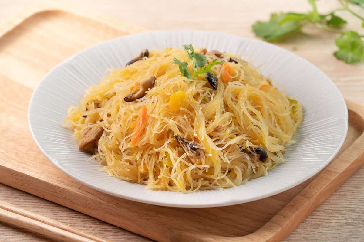 Eating rice vermicelli noodles stir-fried with boiled pumpkin and vegetables on wooden table background.