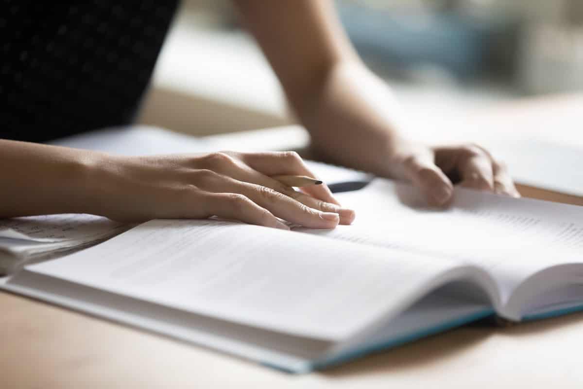 Student preparing for college test, exam, reading book, studying textbook, writing notes, making summary for class report. Learning workplace table, hands with pencil close up