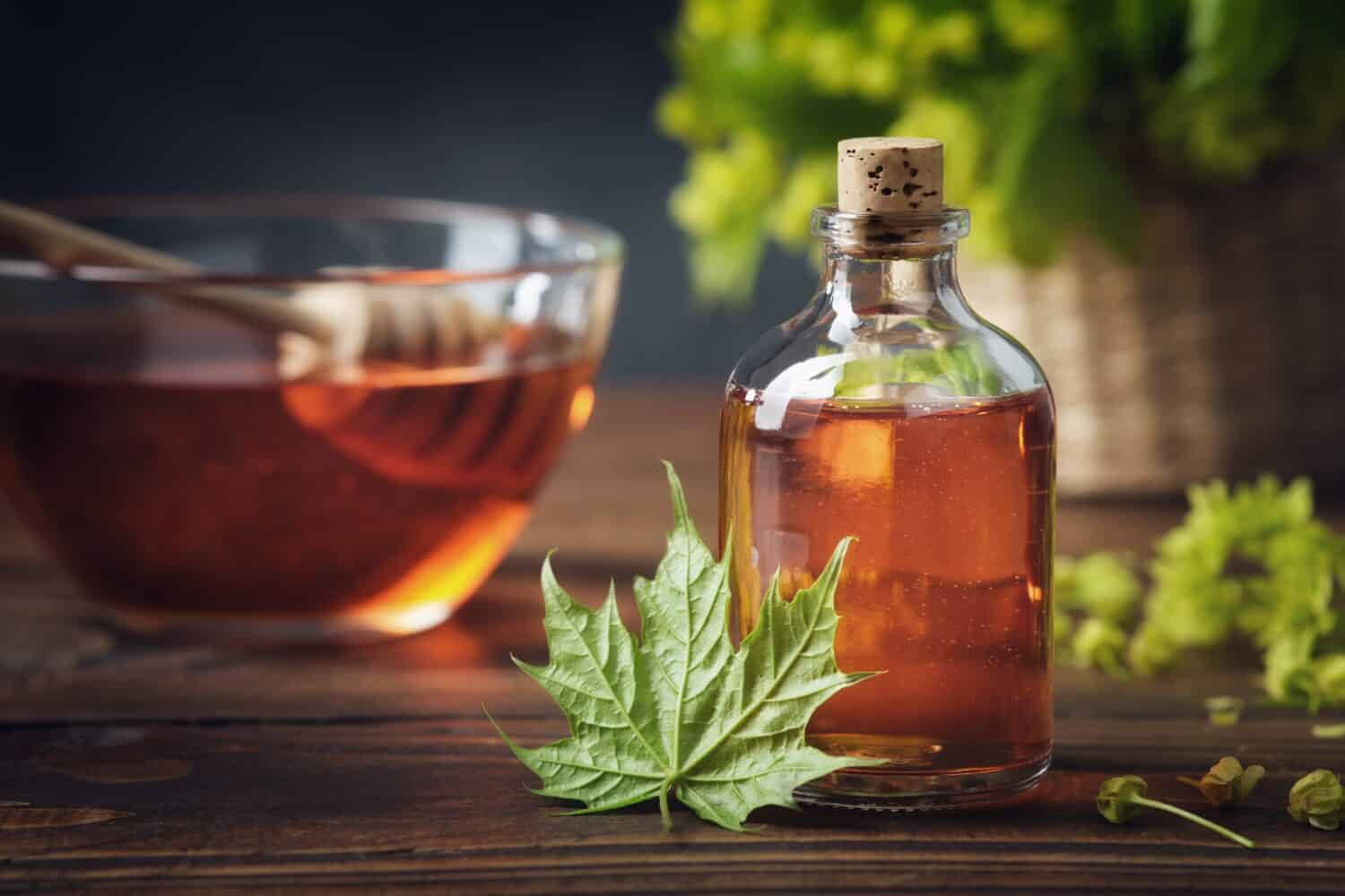 Bottle of maple syrup or healthy tincture and spring maple leaf. Bowl of maple syrup and wooden dipper on background.