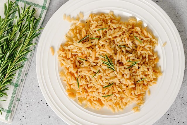 Rice pilaf with orzo, served with fresh rosemary, close up on white plate, flat lay