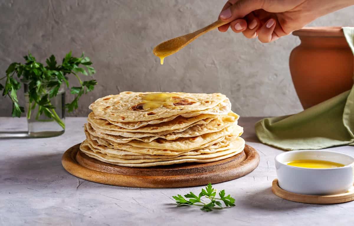 Homemade Indian Chapati or Roti on grey concrete background with human hand pouring butter ghee over