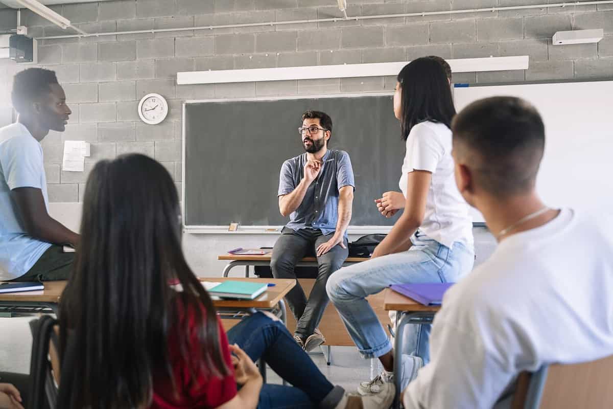 Teenager students listening and talking to friendly young male teacher - Group discussion in High School Education