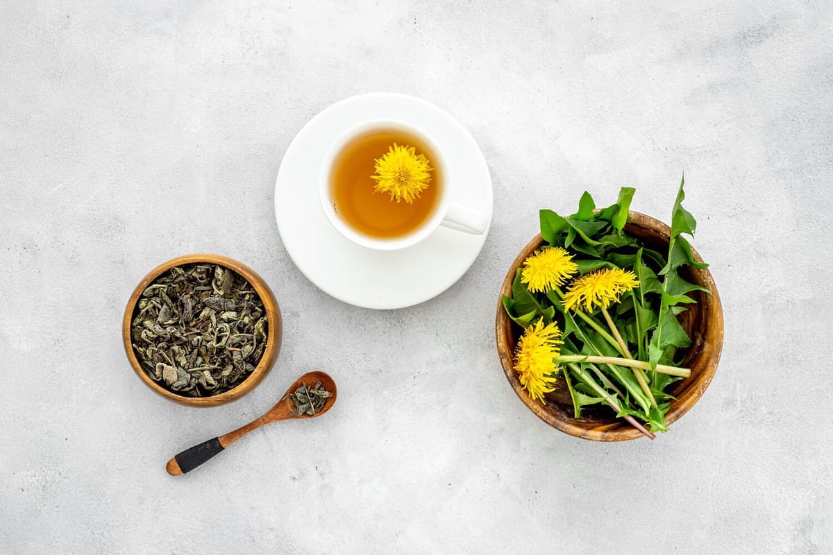 Yellow meadow dandelions with tea and dry leaves in bowl, top view