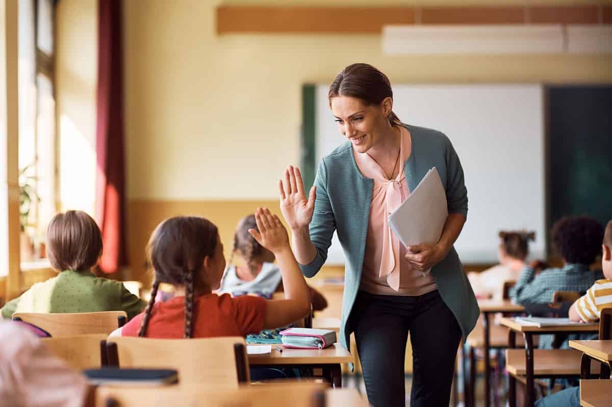 A teacher giving a student a high five in a class. 