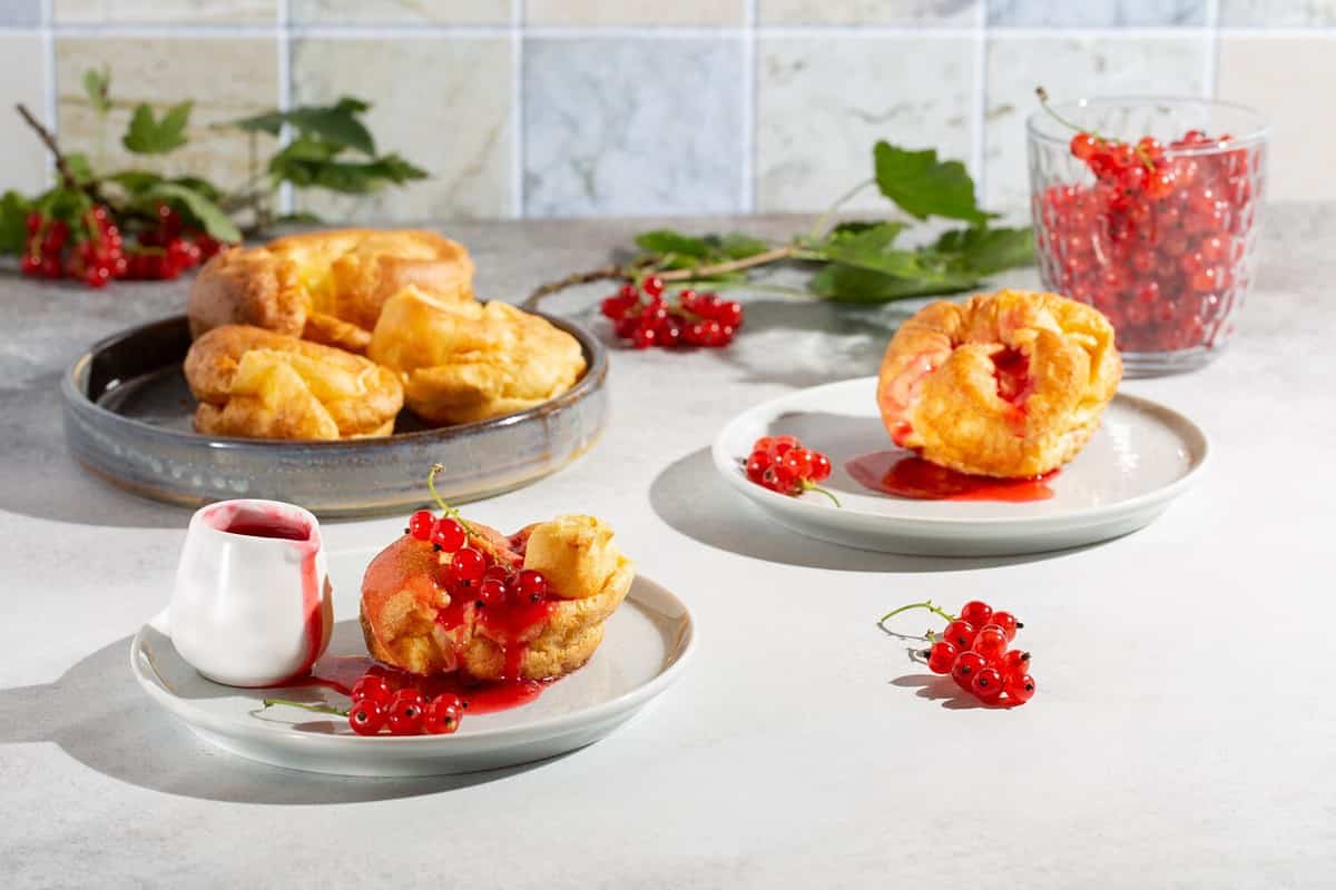 Homemade yorkshire pudding with redcurrant sauce on gray plates on concrete background.