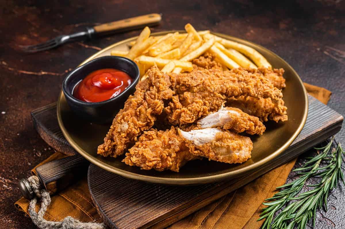 Fried Breaded chicken tender strips with french fries and tomato ketchup on a plate. Dark backgrund. Top view.