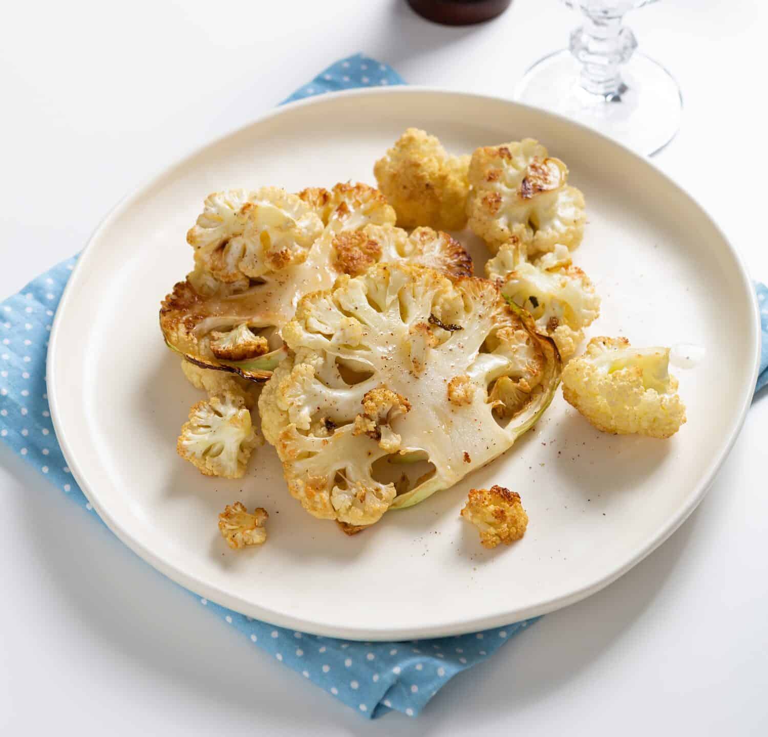 Vegetarian roasted cauliflower steak on white plate close up food