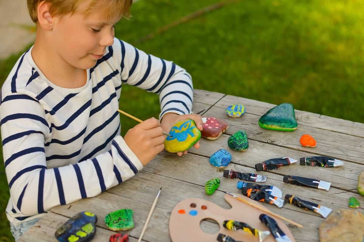 A detailed picture of a child's hands drawing a fungus on a stone with acrylic paints. Home hobbies are authentic. Artwork on stones.