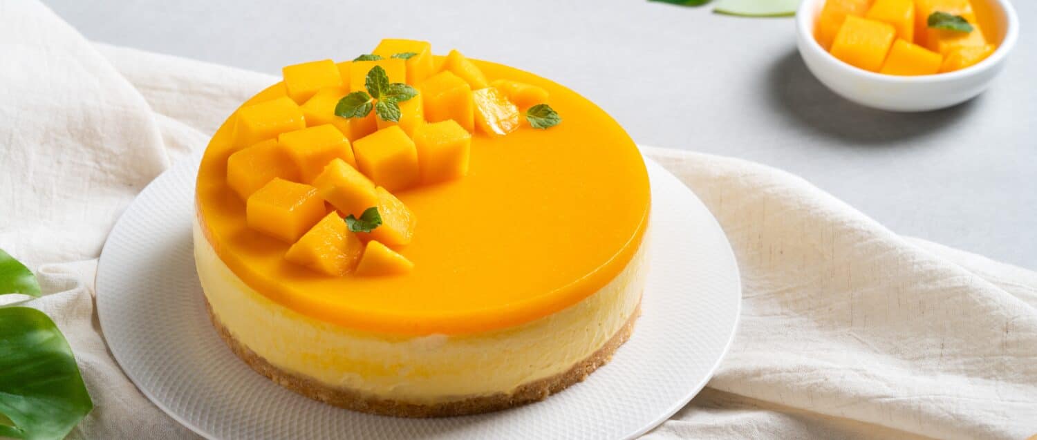 Delicious glazed mango no baked cheese cake with fresh diced mango pulp topping in a plate for serving on bright table background.
