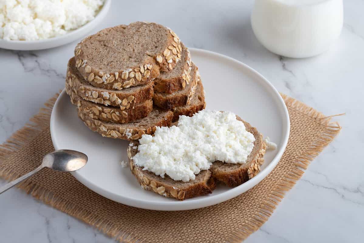 Rye bread and a sandwich with cottage cheese on a white table