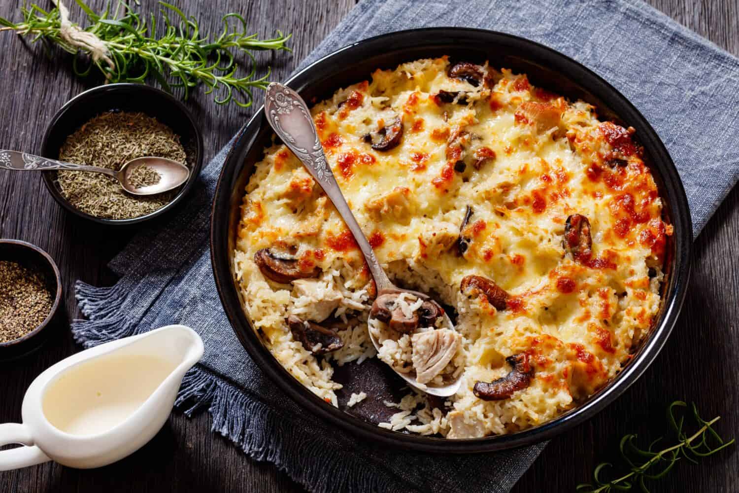 Delicious Chicken Mushroom Rice Casserole in baking dish on dark wood table with ingredients, horizontal view