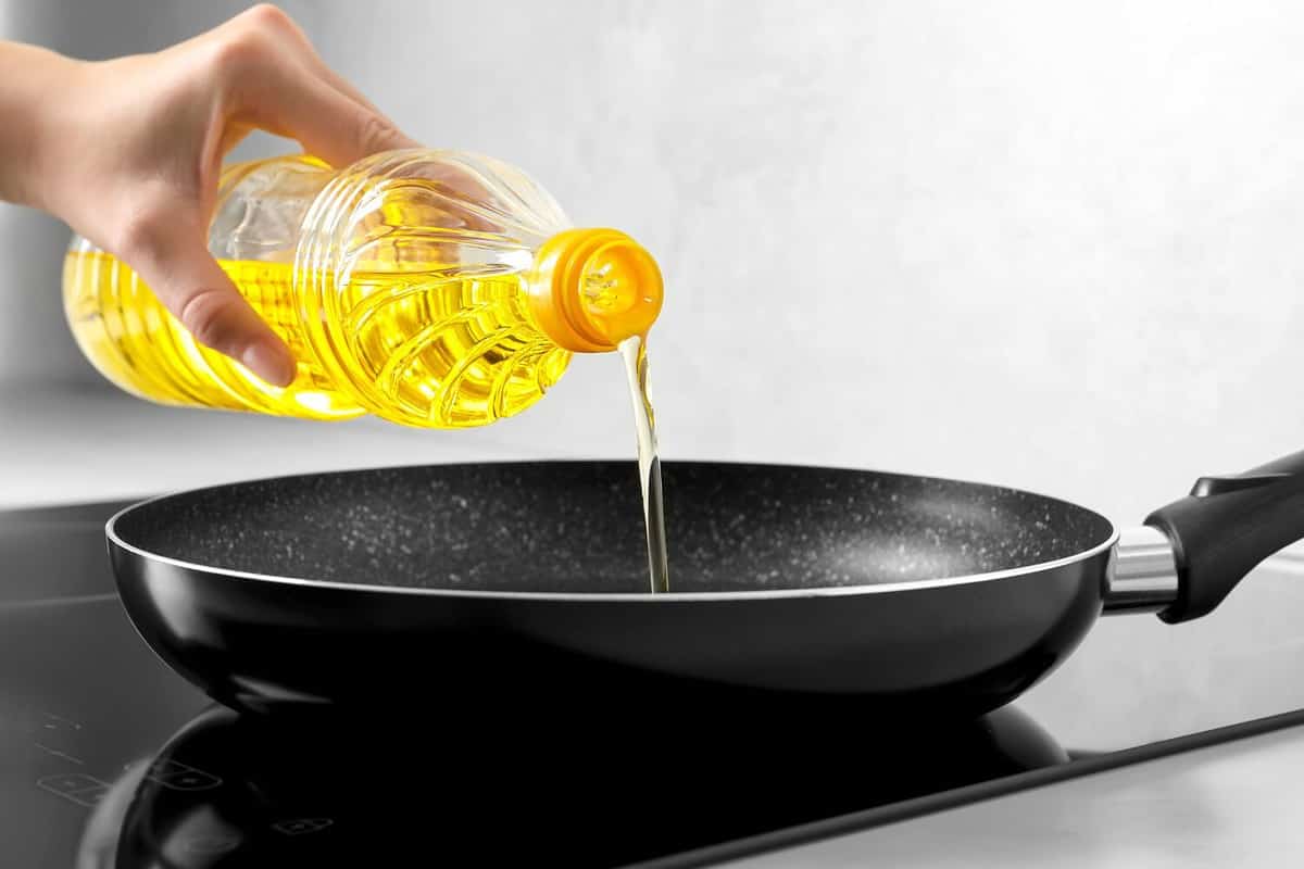 Vegetable oil from bottle into frying pan on stove, closeup