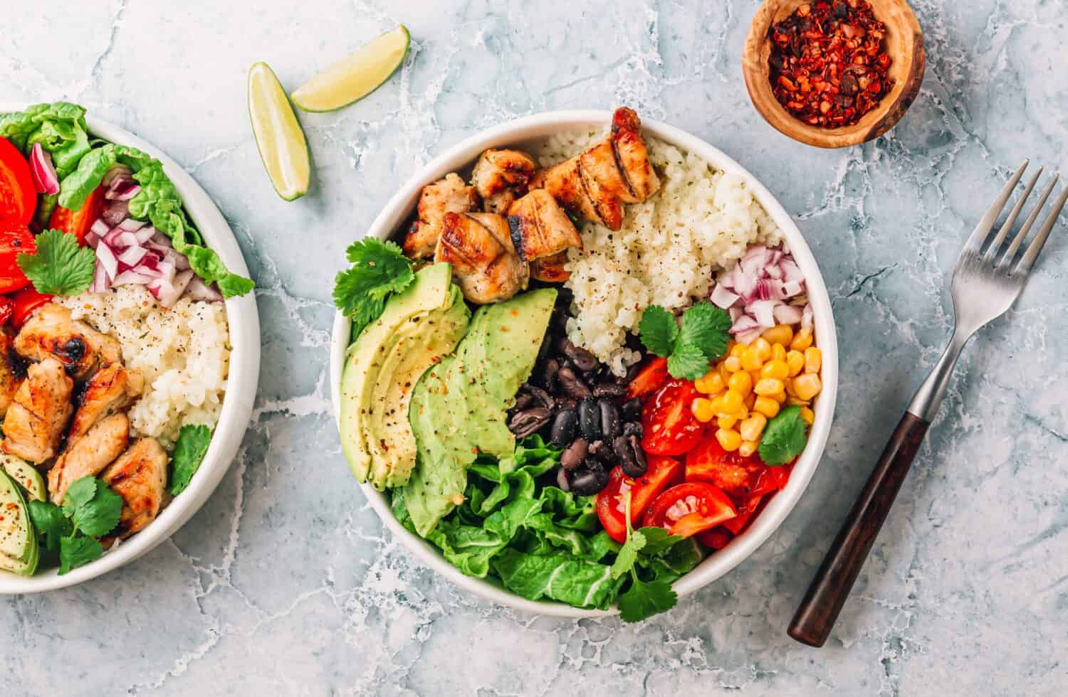 Mexican chicken burrito bowl with rice, beans, tomato, avocado,corn and lettuce.