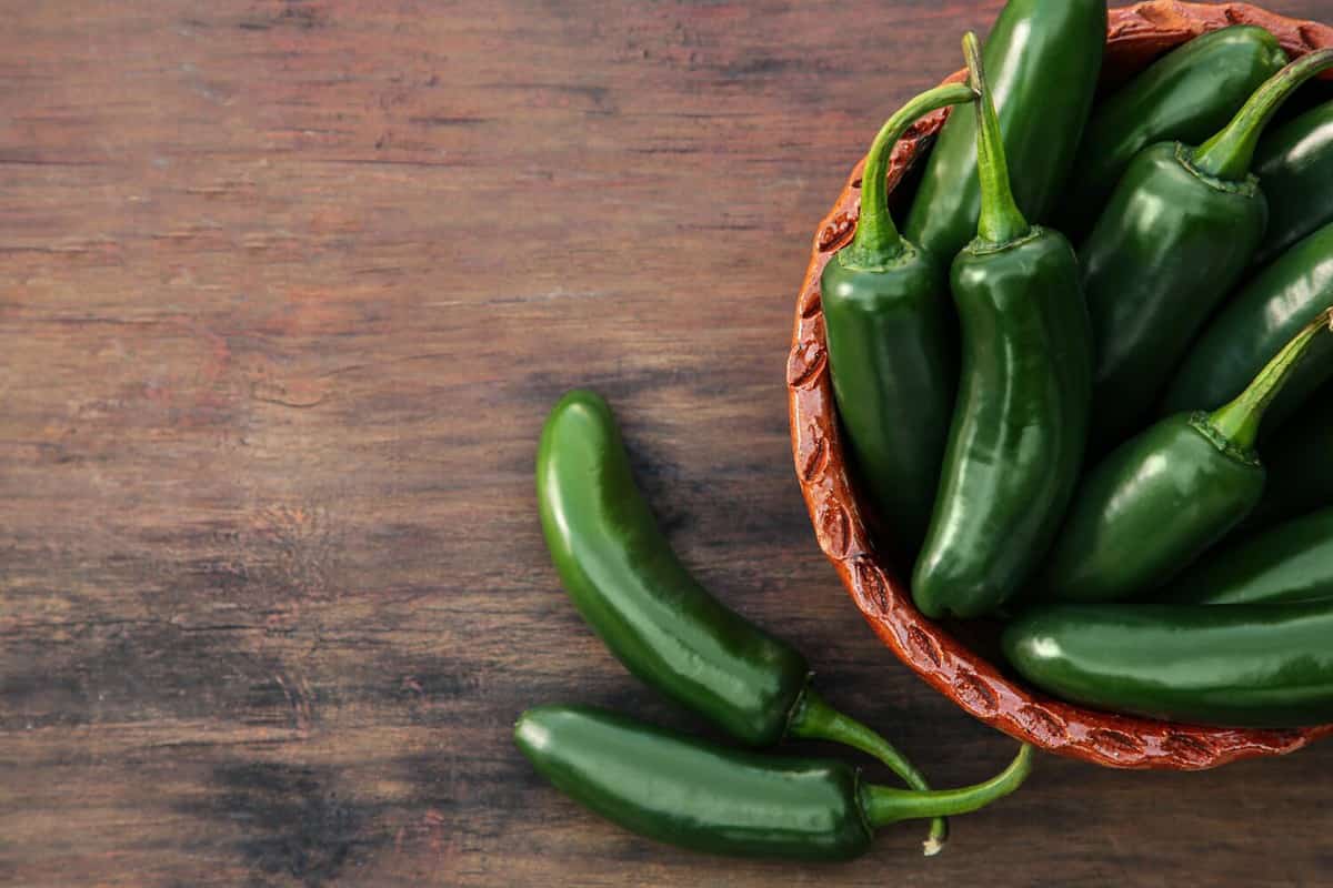 Green jalapeno peppers on wooden table, flat lay. Space for text