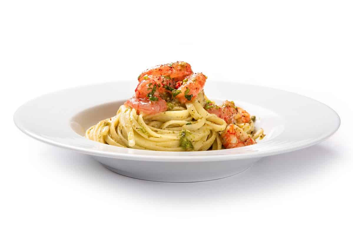 Plate of delicious linguine with pesto and shrimp, italian gourmet pasta isolated on white background