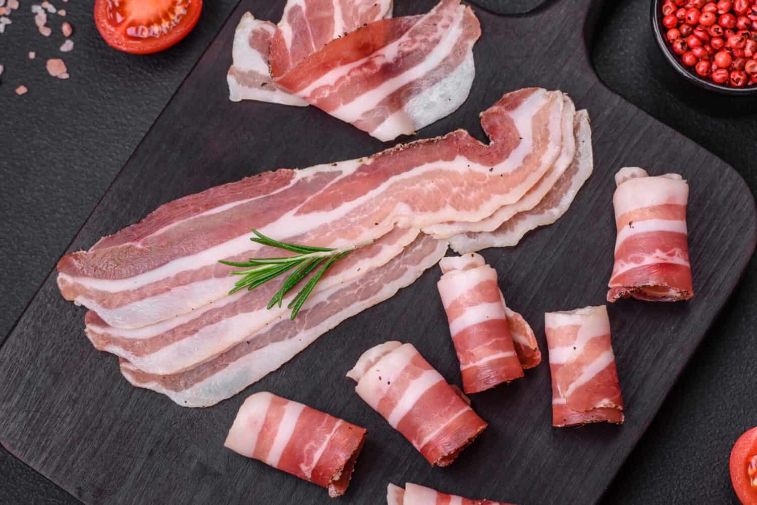 Delicious fresh pancetta with salt and spices cut into thin slices on a dark concrete background