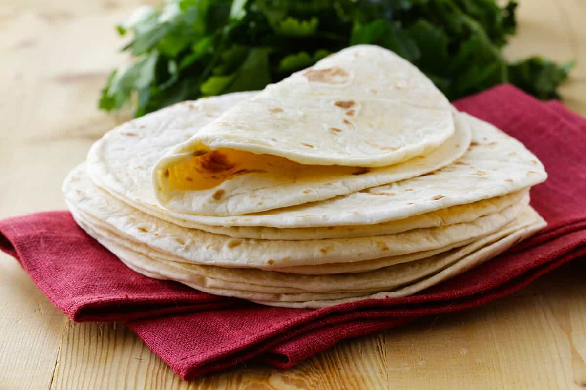 stack of homemade whole wheat flour tortillas on a wooden table