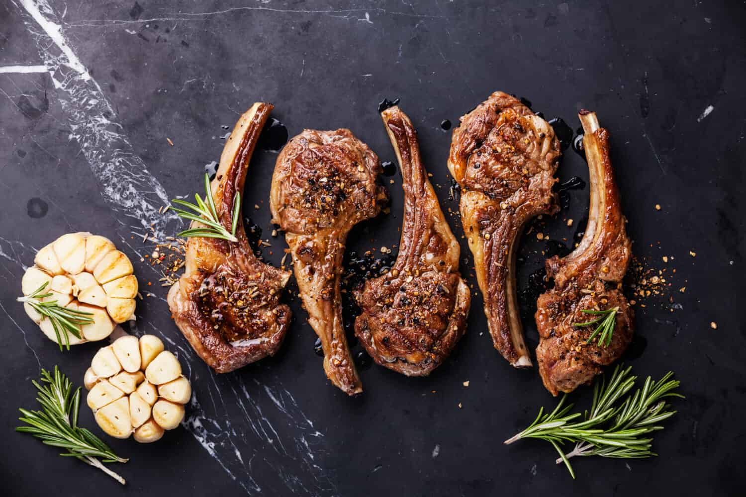 Roasted lamb ribs with spices and garlic on black marble background