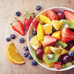 Bowl of healthy fresh fruit salad on wooden background. Top view.