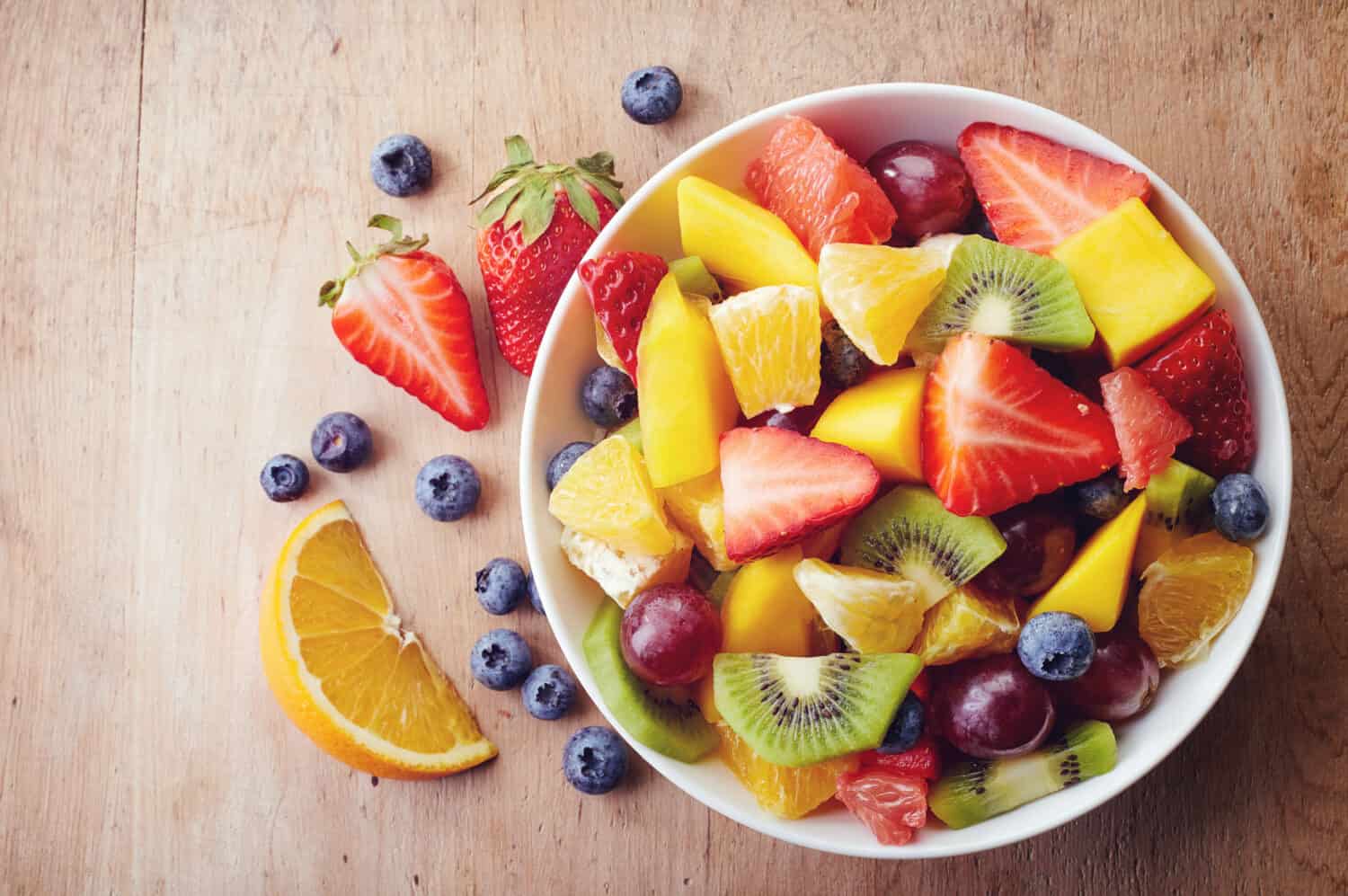 Bowl of healthy fresh fruit salad on wooden background. Top view.