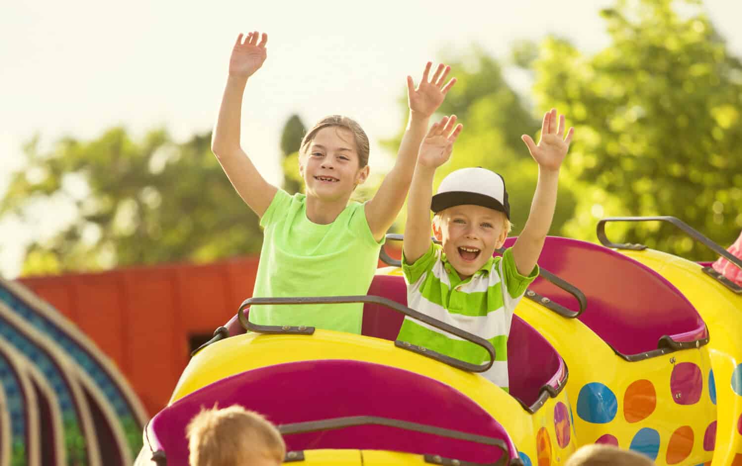 Boy and Girl on a thrilling roller coaster ride at an amusement park with arms raised and yelling with excitement