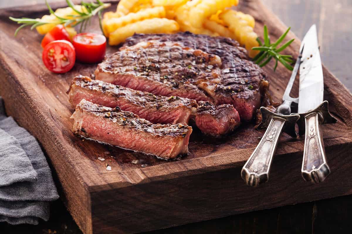Sliced medium rare grilled Steak Ribeye with french fries on serving board block on wooden background