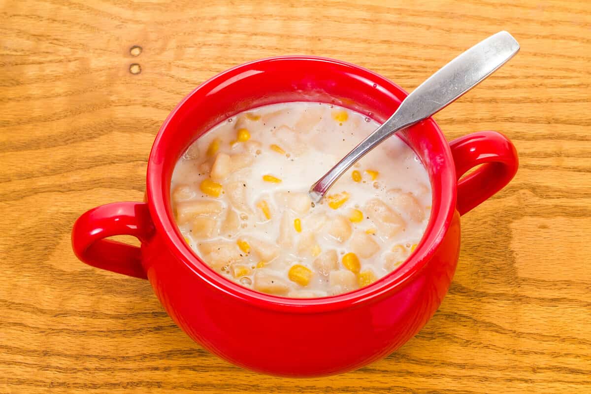 Onions, potatoes and whole grain corn in cream sauce for New England Corn Chowder. Colorful stoneware mug on old wood tabletop.