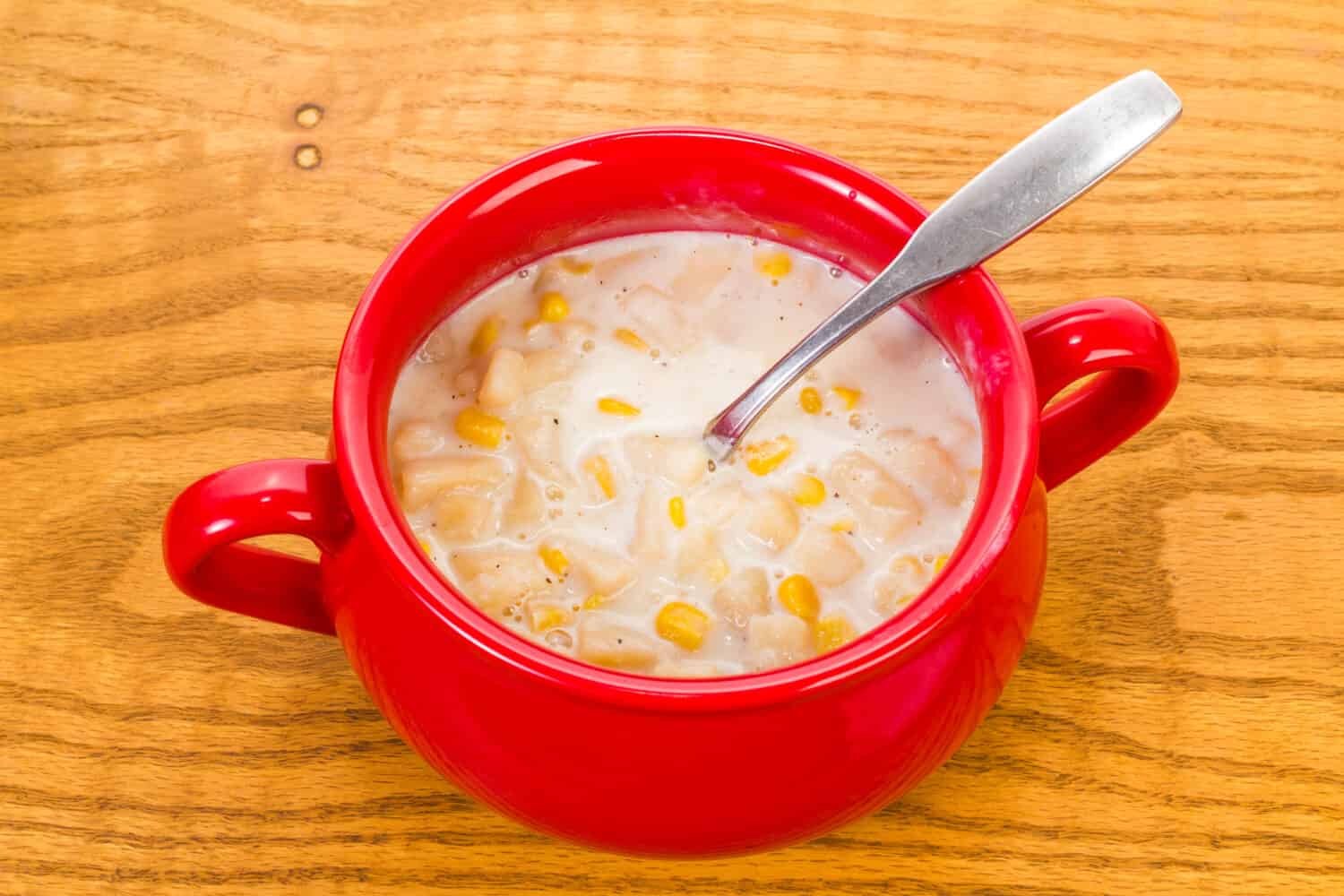 Onions, potatoes and whole grain corn in cream sauce for New England Corn Chowder.  Colorful stoneware mug on old wood tabletop.