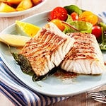 Two portions of fresh grilled pollock or coalfish served with colorful salad and slices of lemon, close up high angle view