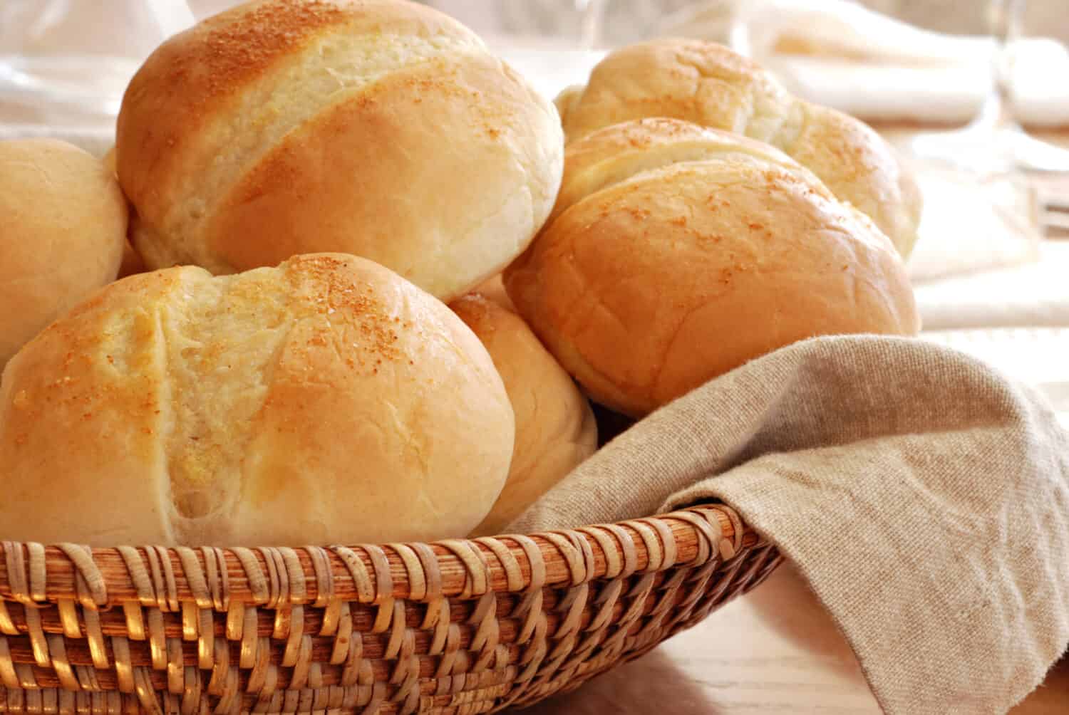 Basket of freshly baked dinner rolls with tableware in background. Macro with shallow dof.