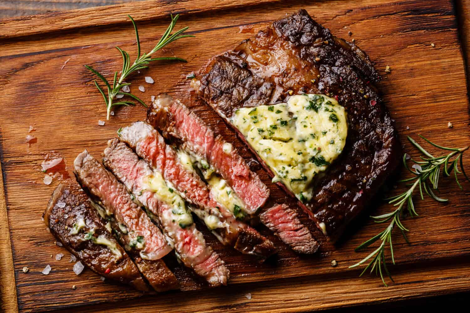 Sliced grilled Medium rare barbecue steak Ribeye with herb butter on cutting board close up