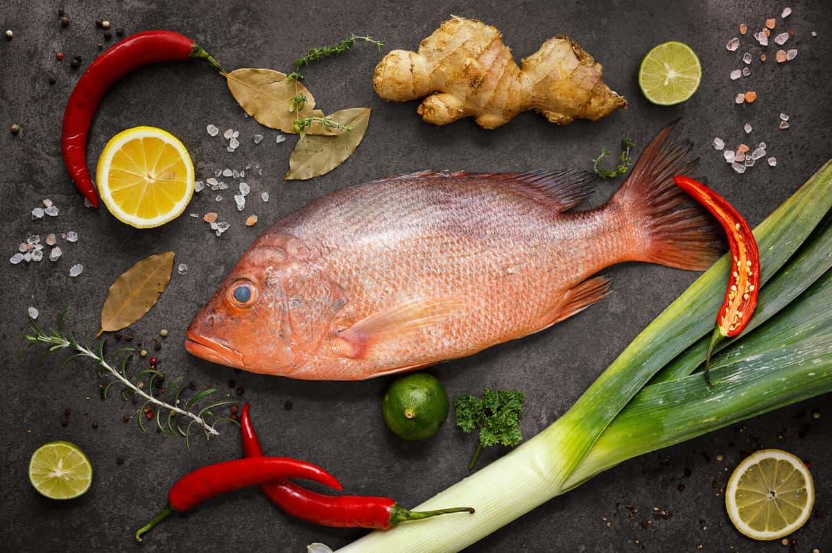 Fresh ingredients to cook fish, red snapper, leak, lime, lemon, parsley, chili pepper, ginger. Top view