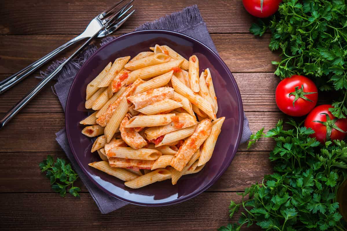 Penne pasta with chicken and tomato sauce on dark wooden background top view. Italian cuisine.