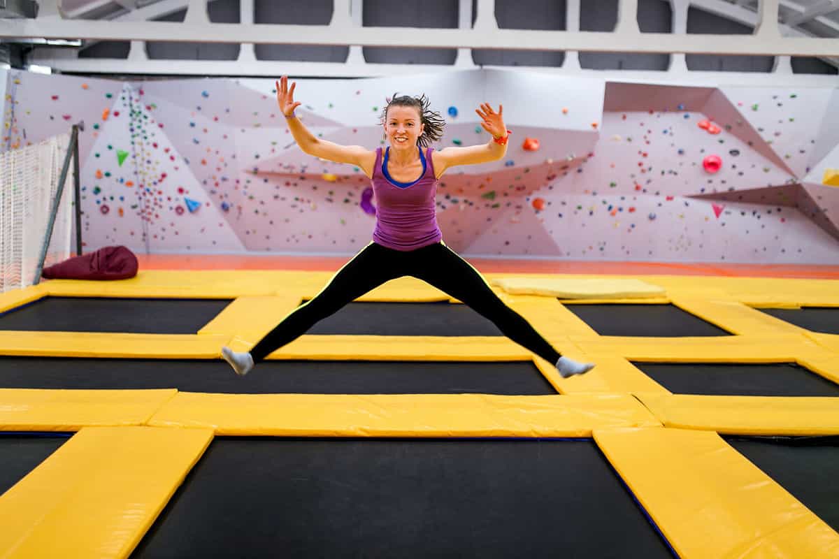 Young sportsman jumping on a trampoline and doing split indoors