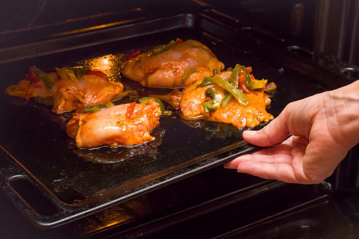 Women's hand holding pan with chicken in curry sauce with peppers and put it in the oven to broil. Daily food.
