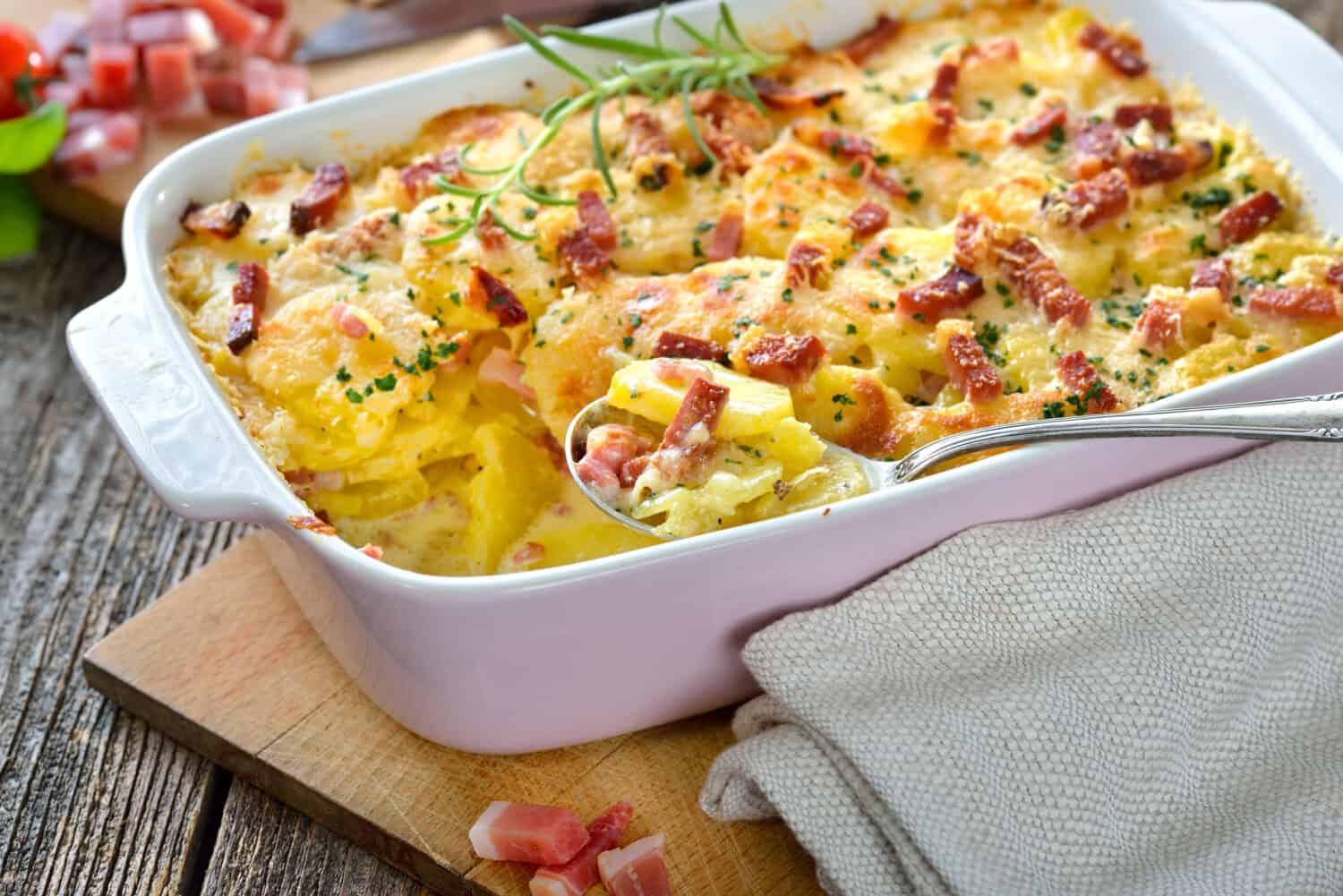Hearty potato gratin with parmesan cheese, cream and delicious cured bacon from South Tyrol freshly served from the oven on a wooden table