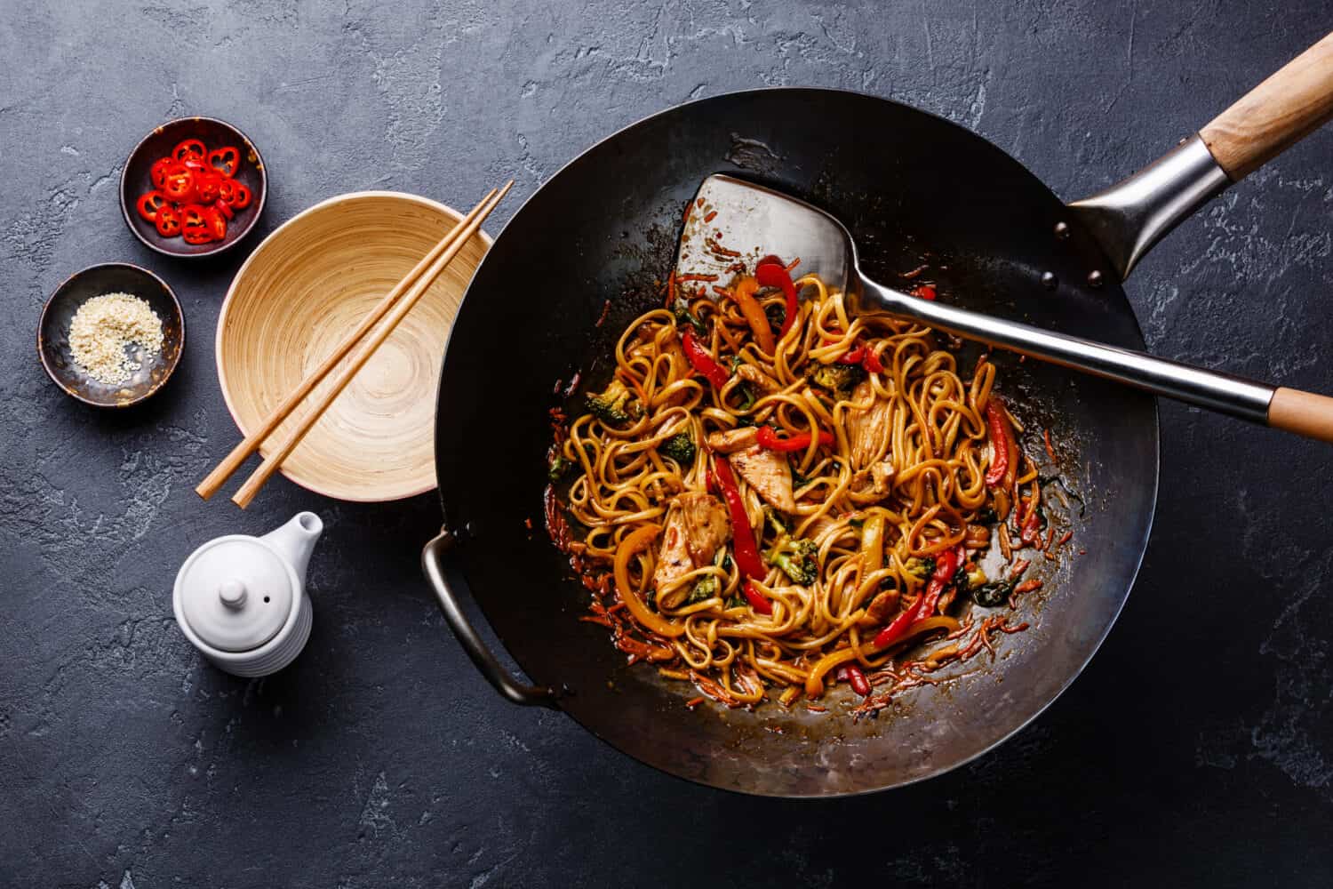 Pan fried noodles with chicken and vegetables in wok pan on dark stone background
