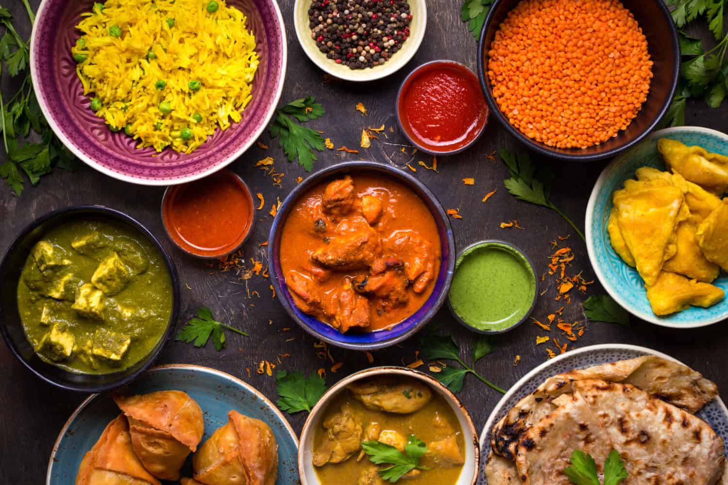 Assorted indian food on dark wooden background. Dishes and appetizers of indian cuisine. Curry, butter chicken, rice, lentils, paneer, samosa, naan, chutney, spices. Bowls and plates with indian food