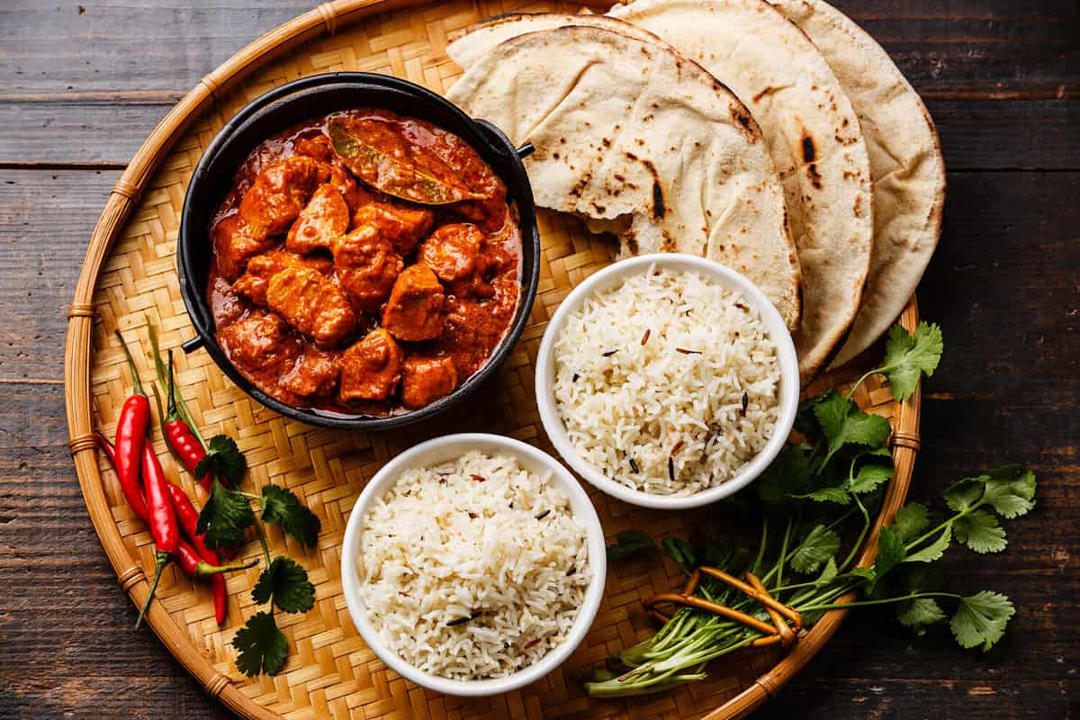 Chicken tikka masala spicy curry meat food in cast iron pot with rice and naan bread close up