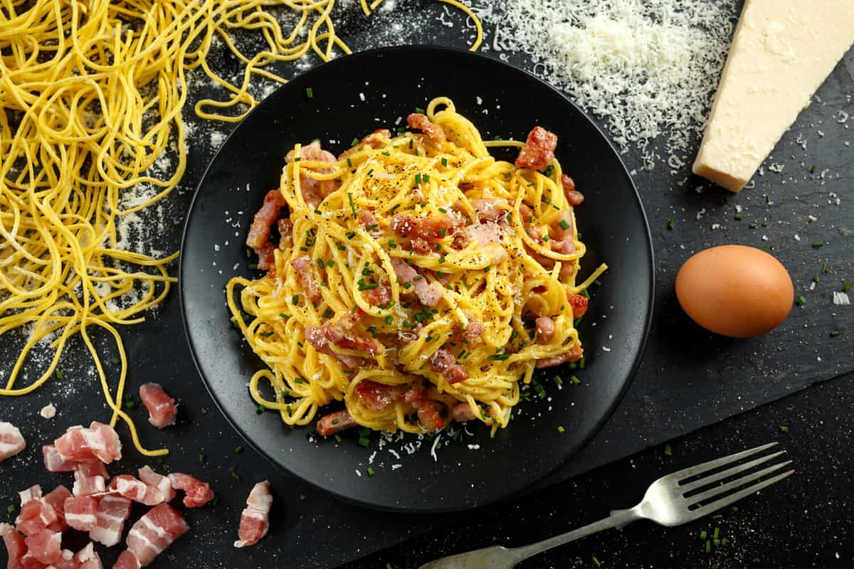 Classic Homemade Pasta carbonara Italian with Bacon, eggs, Parmesan Cheese on black plate.