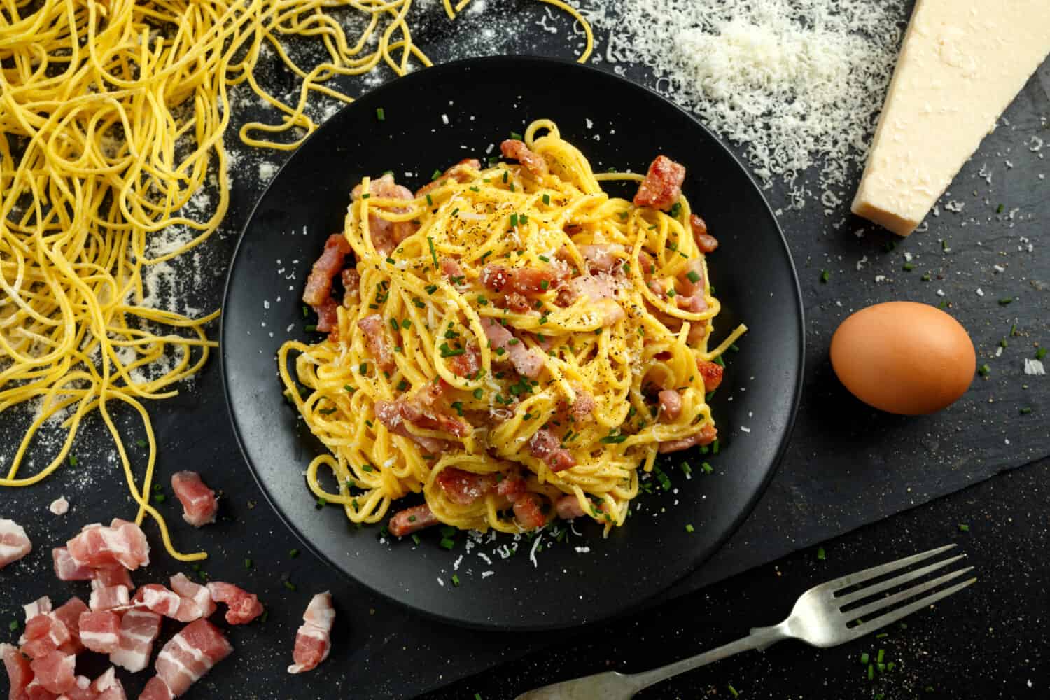 Classic Homemade Pasta carbonara Italian with Bacon, eggs, Parmesan Cheese on black plate.