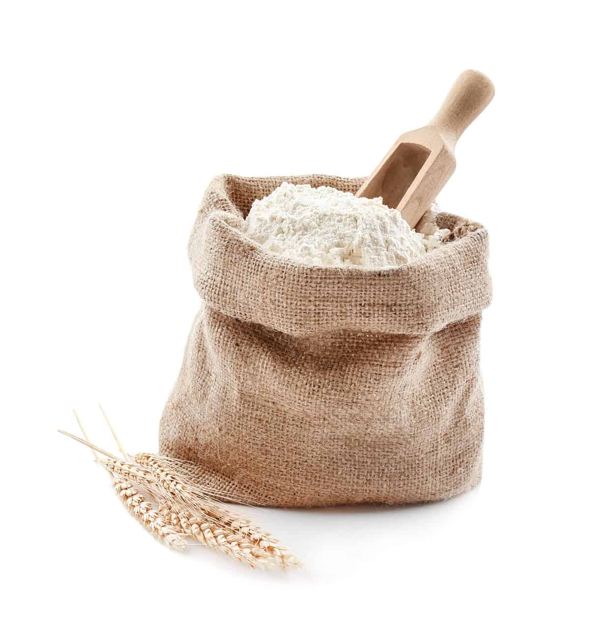 Bag with flour and wooden scoop on white background