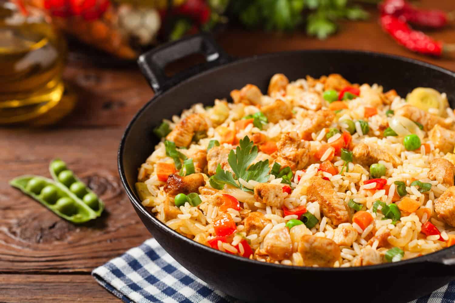 Fried rice with chicken. Prepared and served in a wok. Natural wood in the background. Front view.