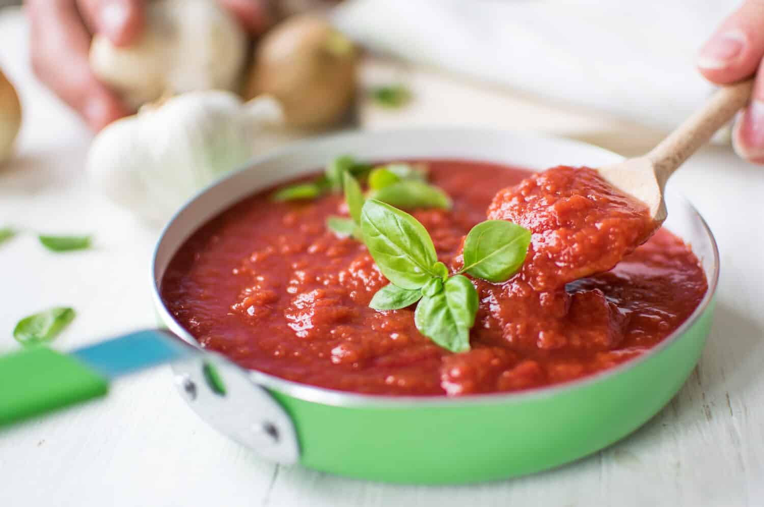 Italian tomato sauce with basil, onion and garlic on white wooden table.