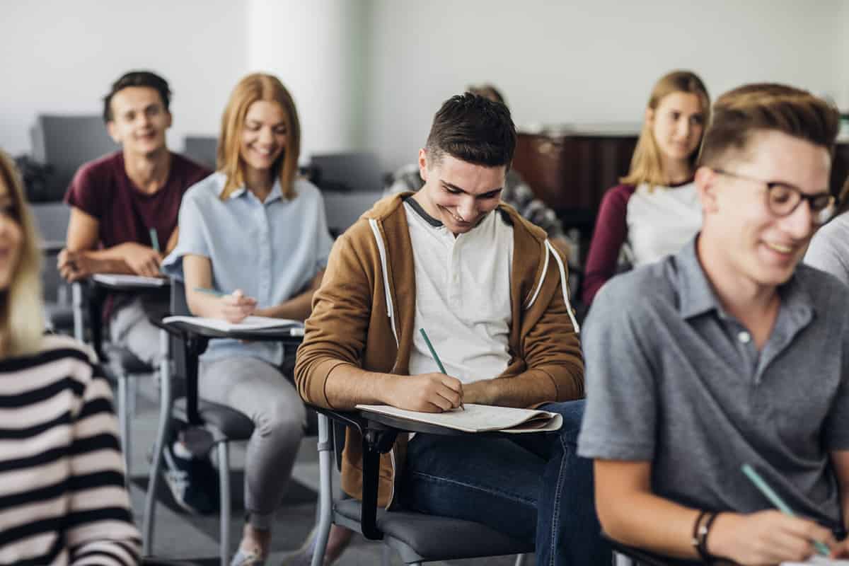 Group of high school students sitting in classroom and writing in notebooks.