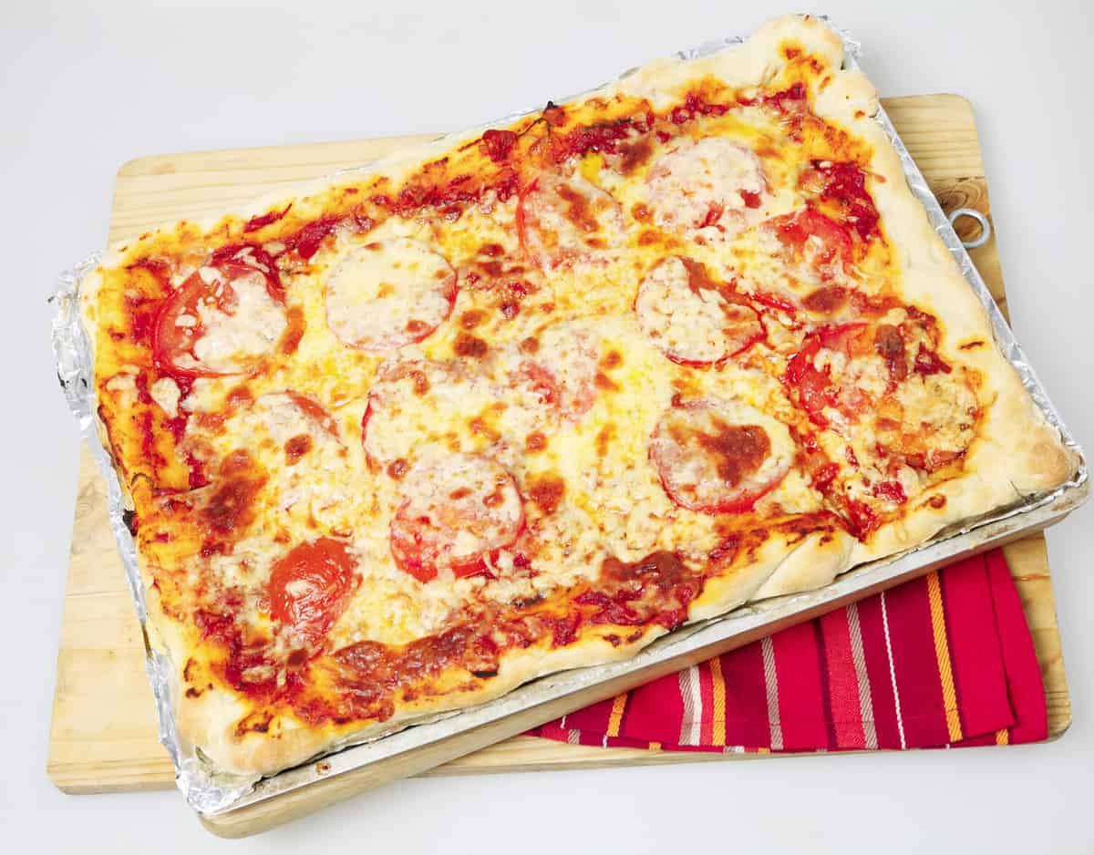 An entire Sicilian rectangular pizza with cheese and tomato topping on a baking sheet
